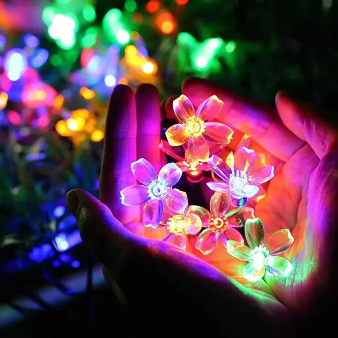 Solar-powered flower-shaped LED Christmas tree lights illuminating a garden at night.