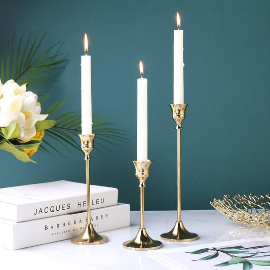 Gold-plated candle holder trio set on a table setting, showcasing small, medium, and large holders with candles.