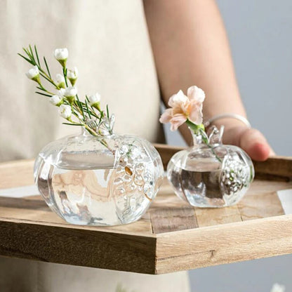 Transparent pomegranate-shaped glass vase with flowers and pebbles, perfect for home or office decoration.