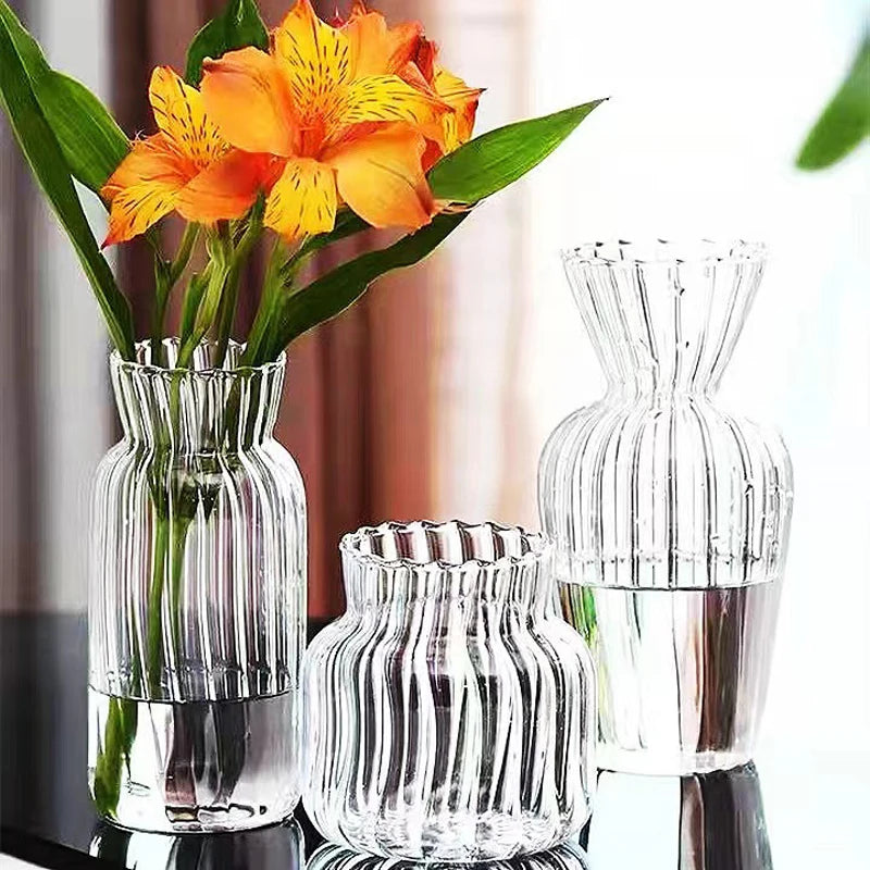 Transparent glass striped hydroponic vase with vibrant orange flowers, styled elegantly on a modern black table.