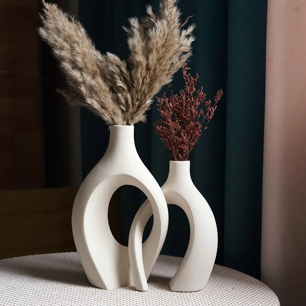 Modern ceramic vase pair featuring interconnecting shapes with a minimalist matte beige finish, displayed on a textured tabletop.