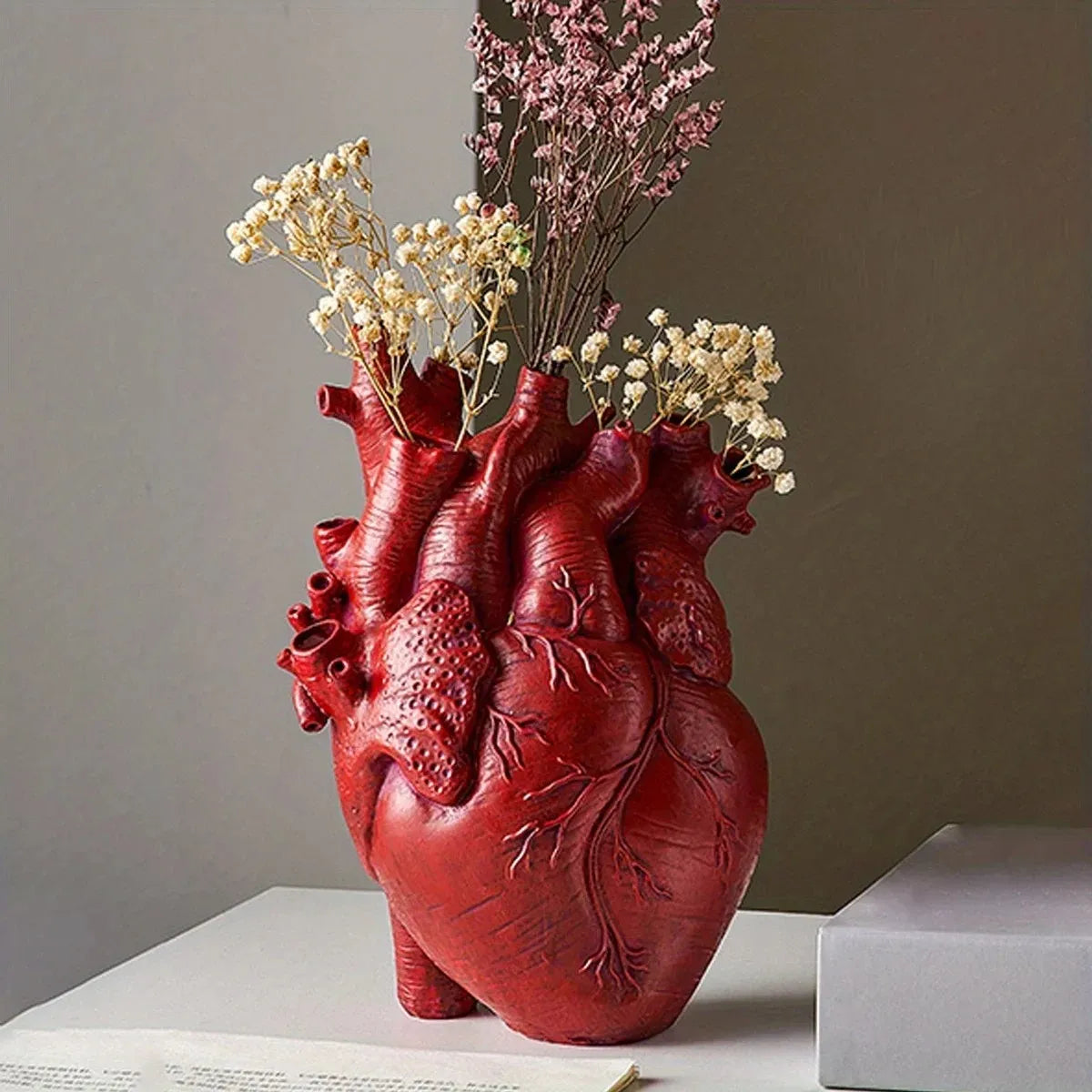 Heart-shaped red art vase holding dried flowers, perfect for modern home decor and artistic displays.