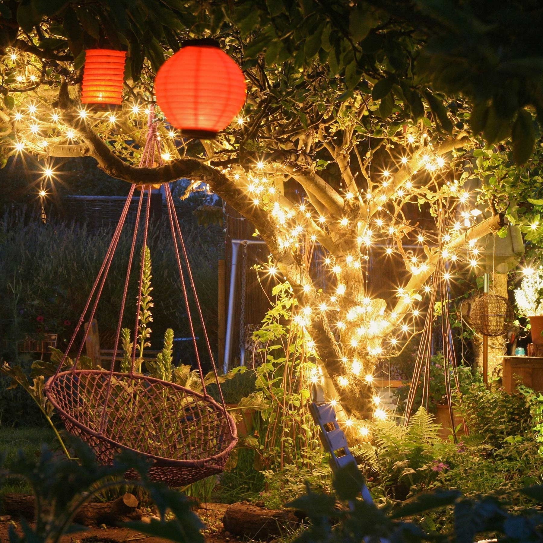 Outdoor garden decorated with solar string fairy lights, wrapped around a tree, casting a warm and magical glow for a cozy ambiance.